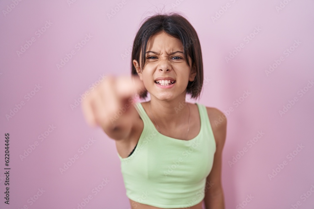 Young girl standing over pink background pointing displeased and frustrated to the camera, angry and furious with you