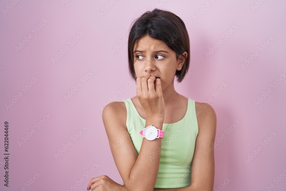 Young girl standing over pink background looking stressed and nervous with hands on mouth biting nails. anxiety problem. Young girl standing over pink background looking stressed and nervous with hands on mouth biting nails. anxiety problem.