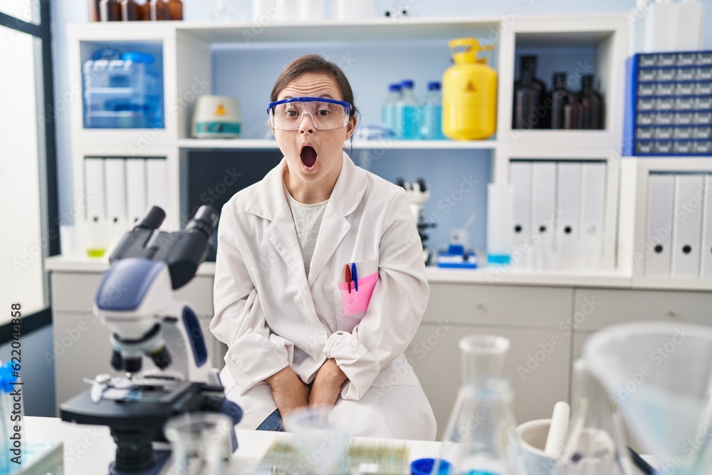 Hispanic girl with down syndrome working at scientist laboratory afraid and shocked with surprise and amazed expression, fear and excited face. Hispanic girl with down syndrome working at scientist laboratory afraid and shocked with surprise and amazed expression, fear and excited face.