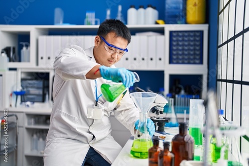 Canvas Print Young chinese man wearing scientist uniform measuring liquid at laboratory