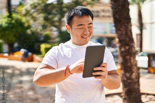Young chinese man smiling confident using touchpad at park
