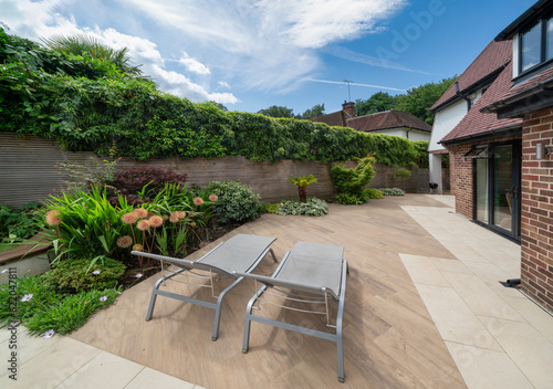 View of stylish, luxury, designer patio and garden with loungers and plants on sunny, summer day.
