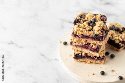 Stack of baked oatmeal squares with fresh blueberry on white tray on marble background with text space