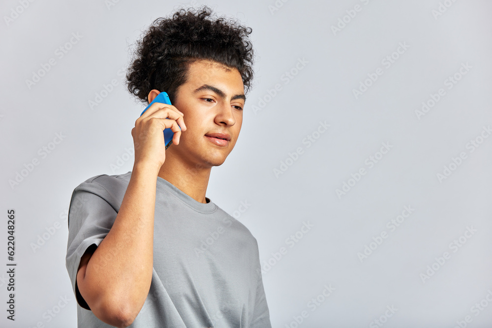 Studio portrait of a young handsome brunette man with curly hair holding a smartphone in his hand. A swarthy guy smiles and talks on a mobile phone. Modern lifestyle. Isolated on a gray background. Studio portrait of a young handsome brunette man with curly hair holding a smartphone in his hand. A swarthy guy smiles and talks on a mobile phone. Modern lifestyle. Isolated on a gray background.