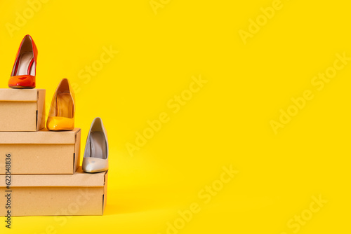 Cardboard boxes with different stylish high-heeled shoes on yellow background