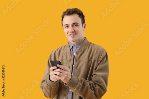 Young man with smartphone on yellow background © Pixel-Shot