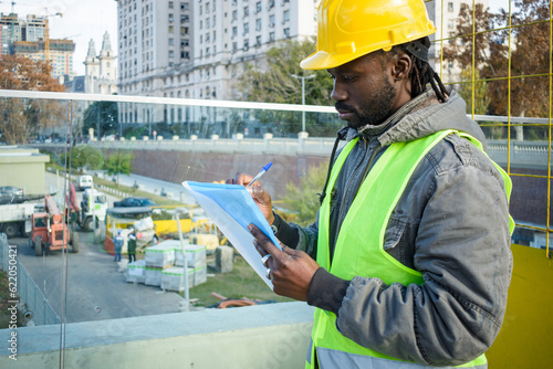 young black engineer man standing supervising the construction site making notes. photo