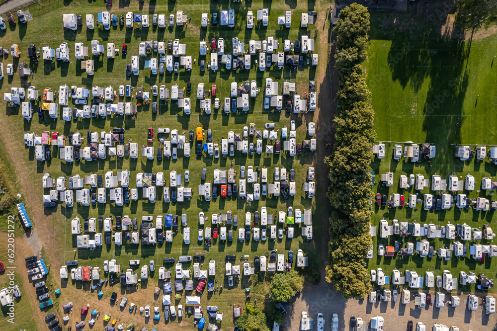 Drone view of a lot of mobile homes, motorhomes, camping vans, tents on a campsite, campground in European village. Holidays, vacation season in summer.