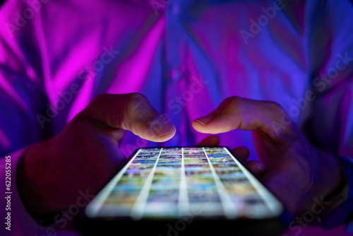 man scrolling mobile phone screen in dark room with neon lights. internet browsing, social media and marketing photo