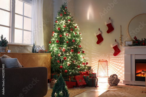 Christmas tree with gifts  glowing lights and fireplace in dark living room