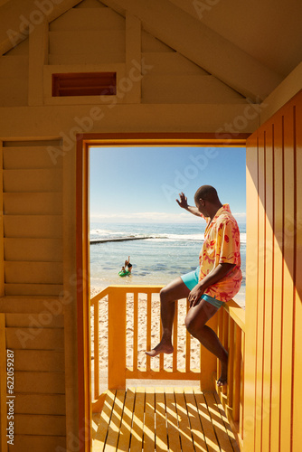 Young father waving at family from beach side cabana in Cape Town