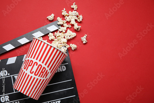 Bucket with tasty popcorn and clapperboard on red background