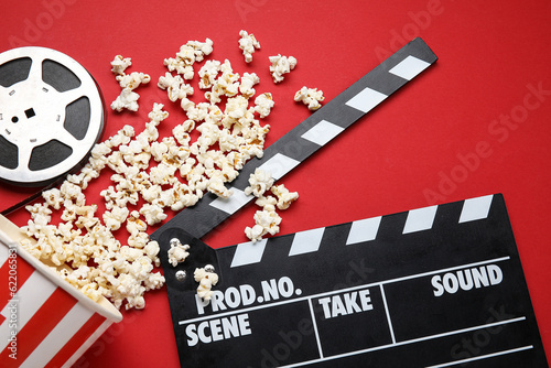 Fotobehang Bucket with tasty popcorn, clapperboard and film reel on red background