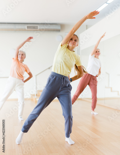 Portrait of cheerful active young girl exercising dance moves in fitness studio