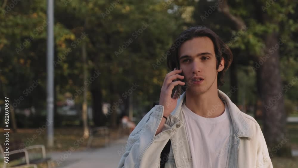 Young man is talking on a cell phone while walking down the street. Positive guy is talking on the phone on the street. Handsome man in the park communicates using a mobile phone. Communication. Young man is talking on a cell phone while walking down the street. Positive guy is talking on the phone on the street. Handsome man in the park communicates using a mobile phone. Communication.