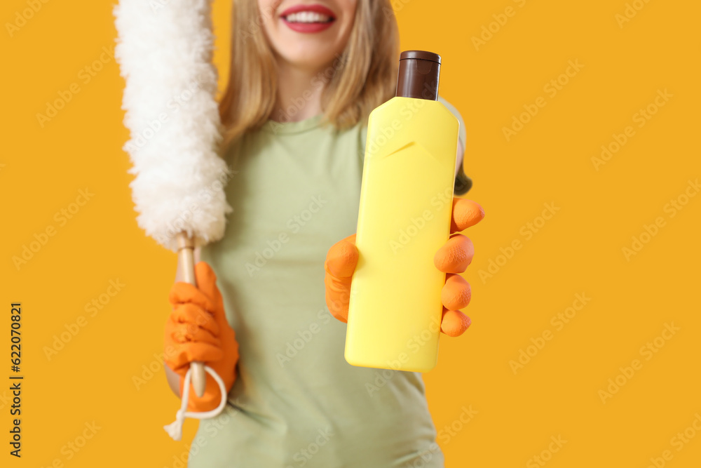 Young woman with bottle of detergent and pp-duster on orange background, closeup Young woman with bottle of detergent and pp-duster on orange background, closeup
