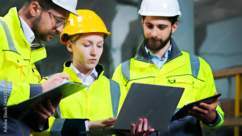Obraz premium Close up of men and woman at construction site talking and discussing work with laptop computer, documents and tablet. Production plant. Males and female co-workers at building. Builders team.