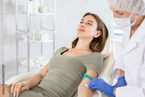 Young female patient having intravenously injection by nurse at treatment room of hospital