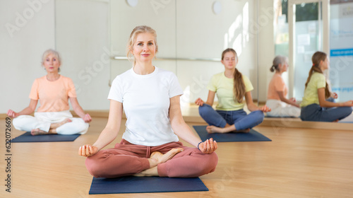 Group of active women and teen girl doing yoga Padmasana exercise, Lotus pose