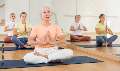 Group of people of different ages sitting in lotus position practicing meditation in yoga class