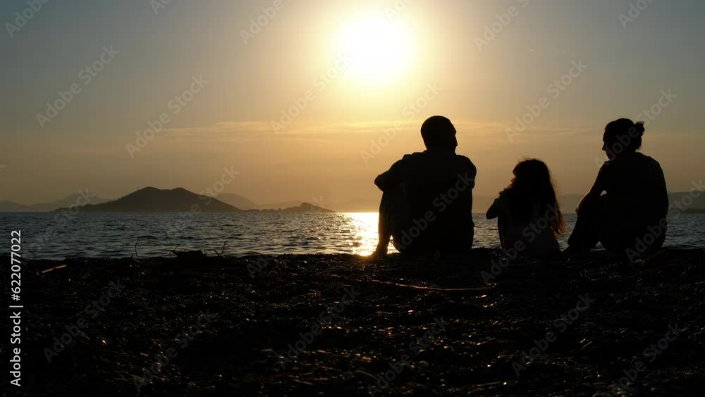 Family on the seashore enjoying the sunset. Silhouette mother, father and daughter sitting at sunset on the beach. Family on the seashore enjoying the sunset. Silhouette mother, father and daughter sitting at sunset on the beach.