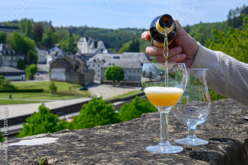 Pouring of blond strong Belgian abbey beer in to glass in sunny day with nice view on old town Bouillon, Belgium photo