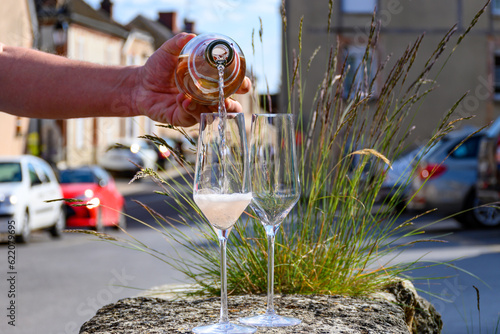 Pouring of premier cru sparkling rose wine with bubbles champagne with view on old houses of Hautvillers, where lived Benedictine monk how developed champagne wine, France.