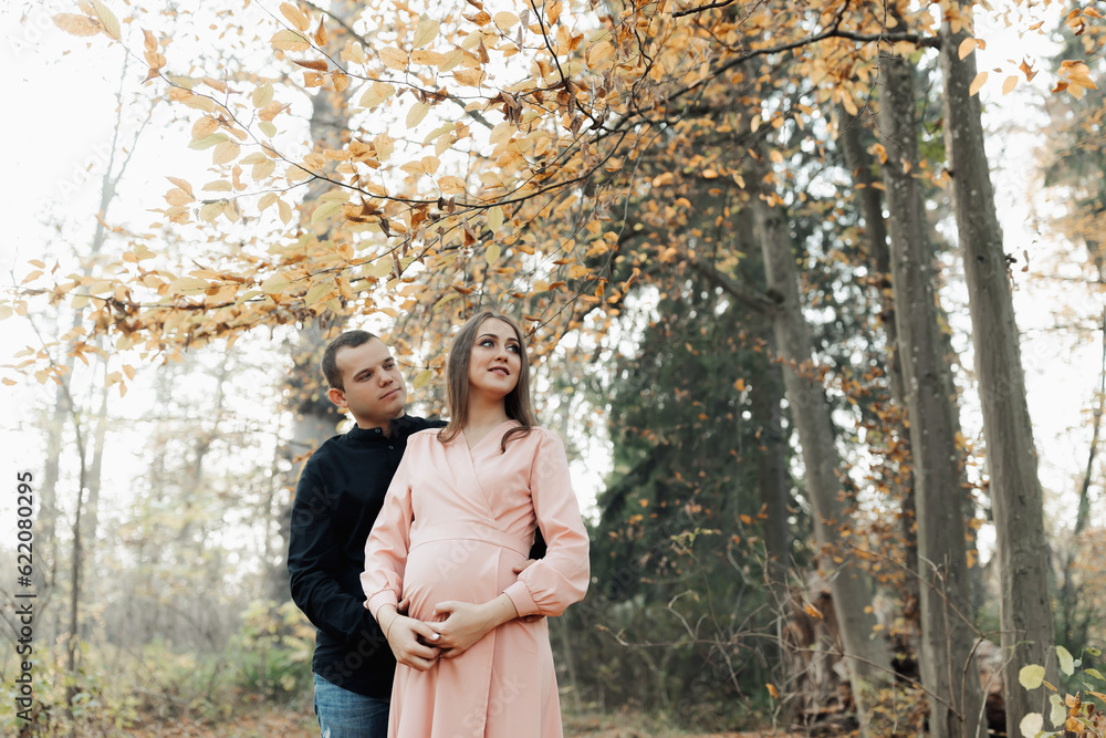 Fototapeta premium A man and his pregnant wife embrace in the forest at sunset, waiting for the birth of a child. Happy family concept.