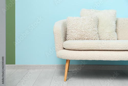 Cozy white sofa with pillows near blue wall © Pixel-Shot