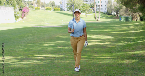 Smiling friendly woman golfer walking on the fairway on the golf course approaching the camera with a happy grin
