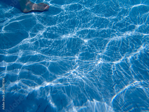 Underwater foot walking on blue pool bottom with ripples