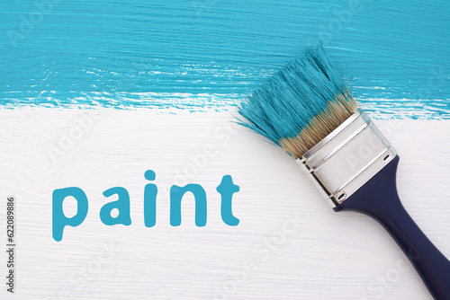 Stripe of turquoise paint with a paintbrush and the word PAINT on a white wooden board