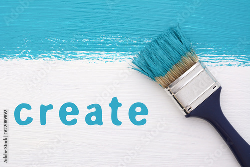 Stripe of turquoise paint with a paintbrush and the word CREATE on a white wooden board