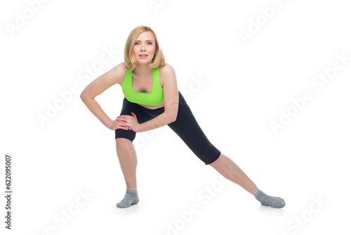 Beautiful middle aged blond fit woman in green bra top and black pants doing sport exercise. Isolated over white background. Copy space.