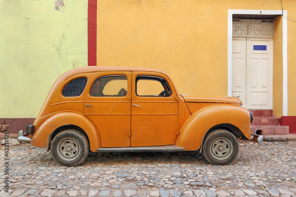 Old orange car with a colorful facade in the background in a Cuban town 