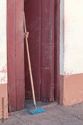 A lady hiding behind a door and holding a broom