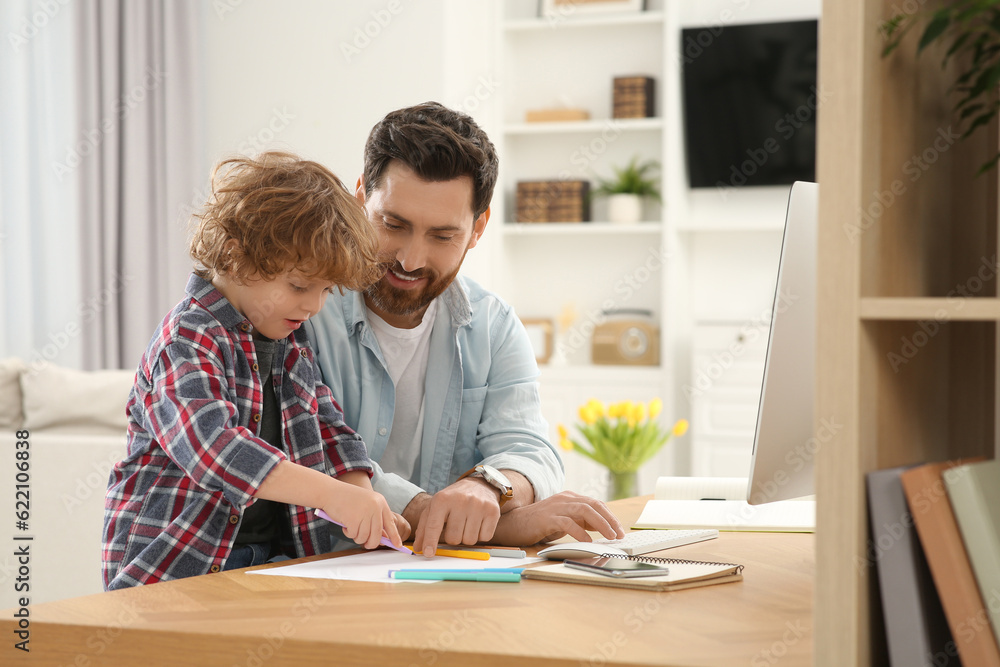 Man working remotely at home. Father looking onto his son's drawing at desk Man working remotely at home. Father looking onto his son's drawing at desk