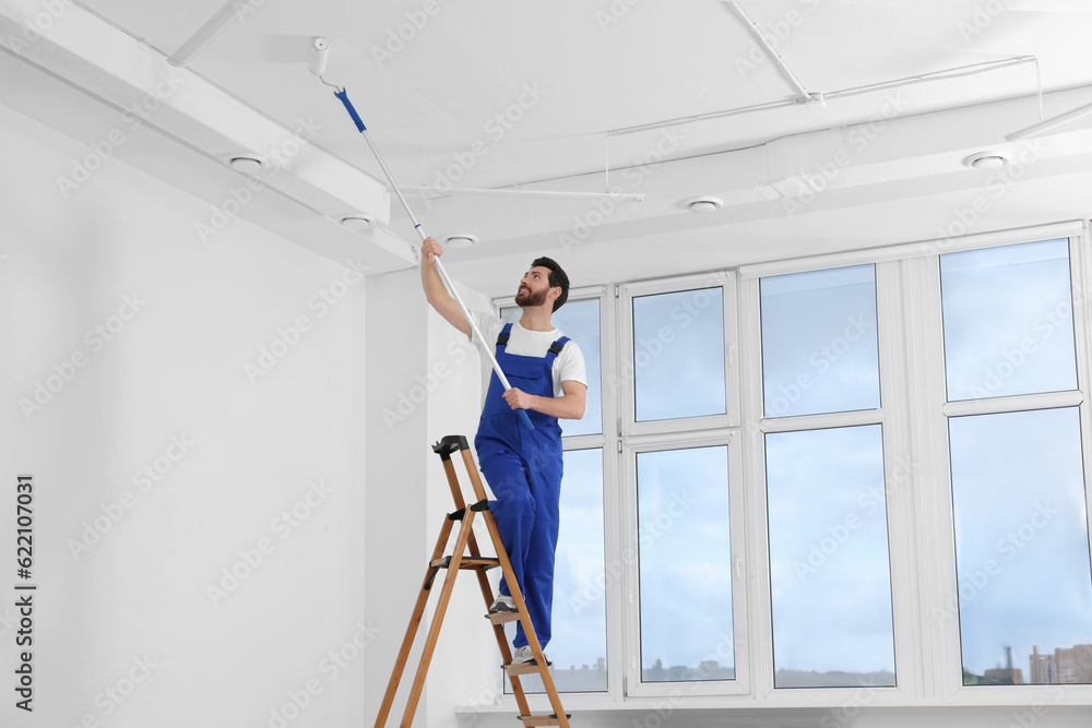 Handyman painting ceiling with roller on step ladder in room Handyman painting ceiling with roller on step ladder in room