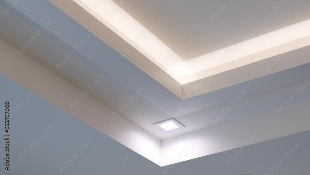 Drywall multi-level white ceiling with built-in led light and halogen lamp in new apartment. Modern design with fluorescent lighting Drywall multi-level white ceiling with built-in led light and halogen lamp in new apartment. Modern design with fluorescent lighting