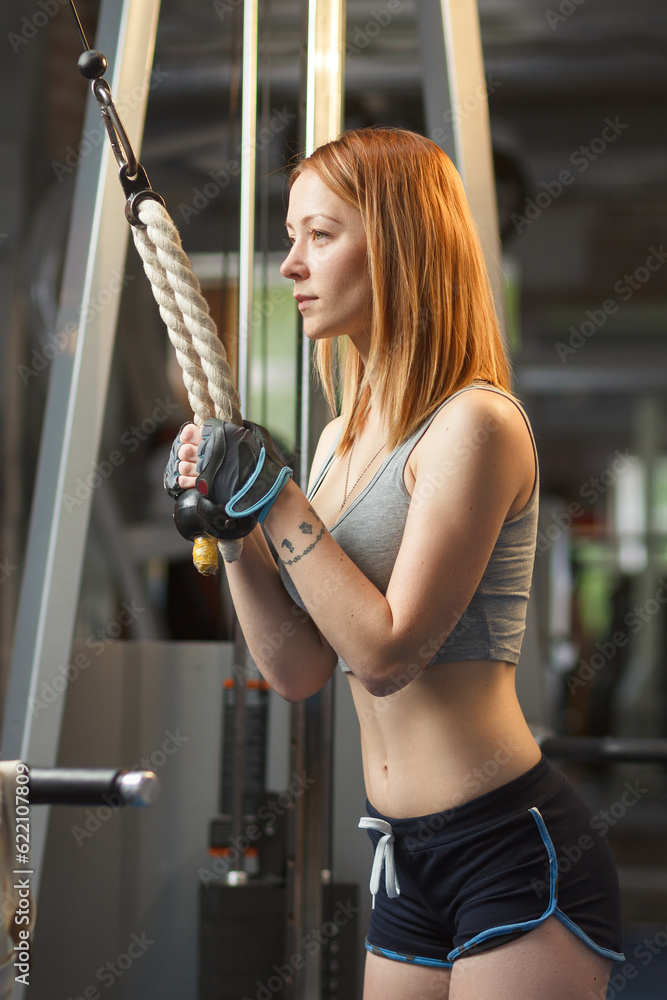 Concept: sport, healthy lifestyle. Young strong girl does exercises on cable crossover machine Concept: sport, healthy lifestyle. Young strong girl does exercises on cable crossover machine