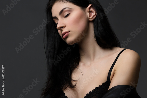 Picture of beautiful brunnette model woman in lingerie or underwear posing with her eyes closed isolated on black background in studio.