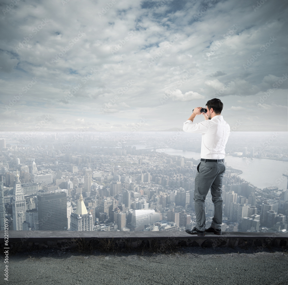 Businessman looks at the city from the roof with binoculars Businessman looks at the city from the roof with binoculars