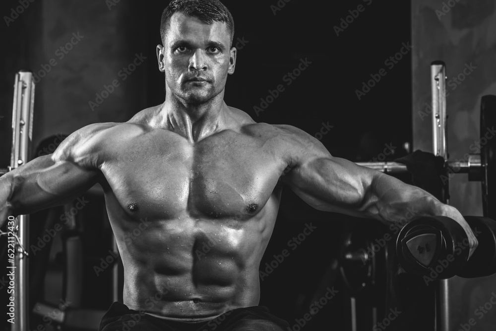 Brutal athletic man pumping up muscles with dumbbells in monochrome