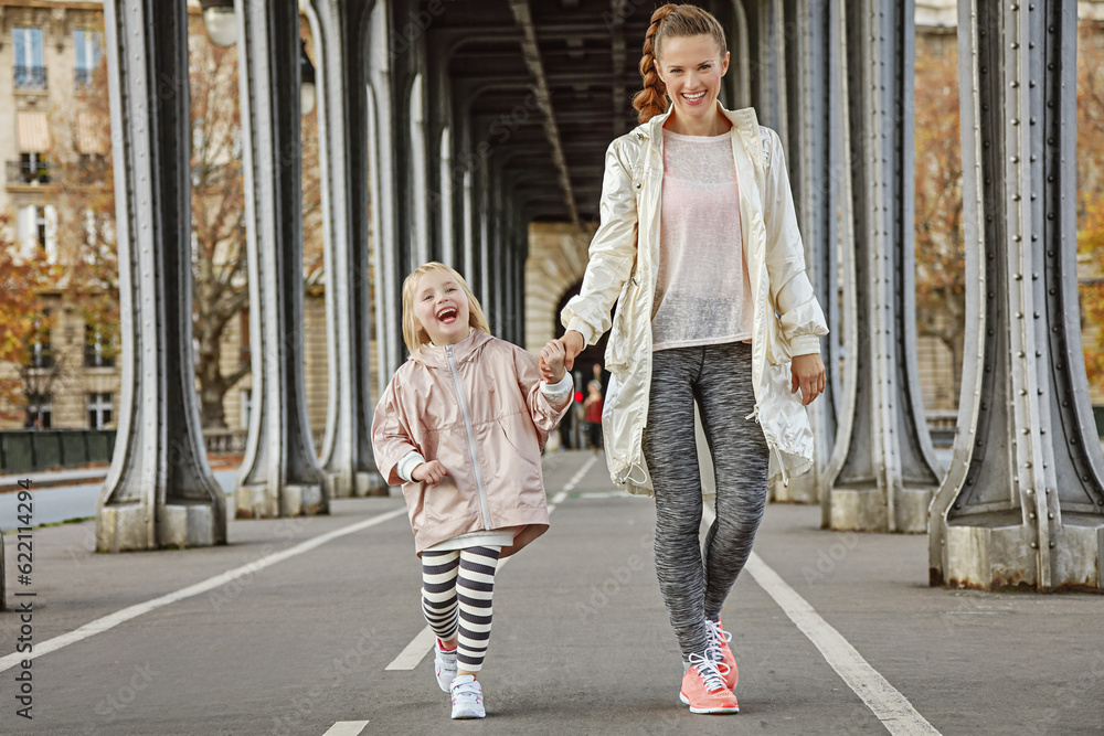 Year round fit & hip in Paris. Full length portrait of happy active mother and child in sport style clothes on Pont de Bir-Hakeim bridge in Paris walking