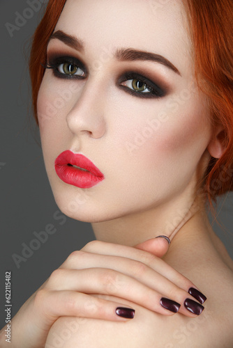 Beautiful young woman with smoky eyes and full red lips. Hands with dark nail polish. Studio beauty shot over blue background. Copy space.