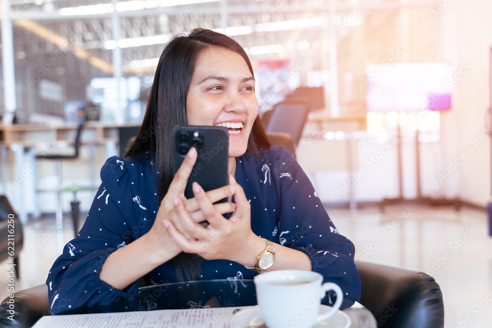 Smiling asian woman sitting on couch at office using smartphone ...