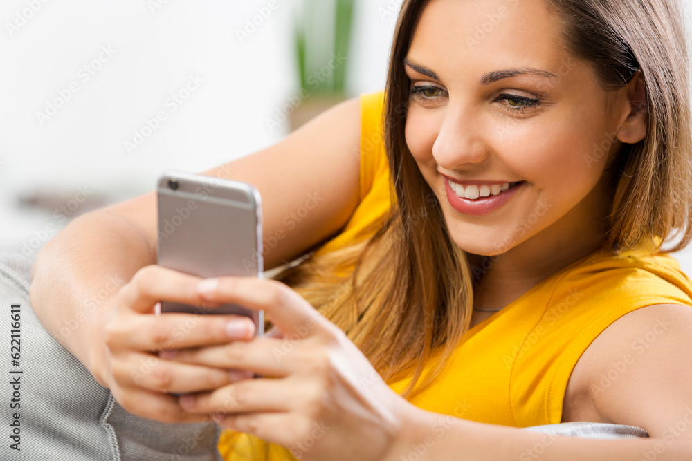 Beautiful young woman sitting on a sofa and send text messages Beautiful young woman sitting on a sofa and send text messages