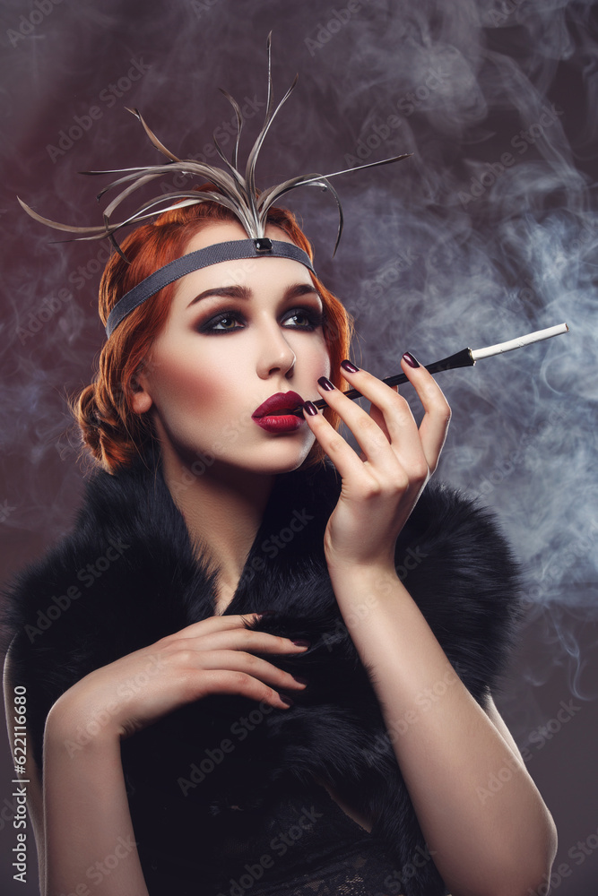 Obraz premium Beautiful young woman with smoky eyes and full red lips holding cigarette holder. Vintage head piece. Retro styling. Studio beauty shot over smoky background. Copy space.