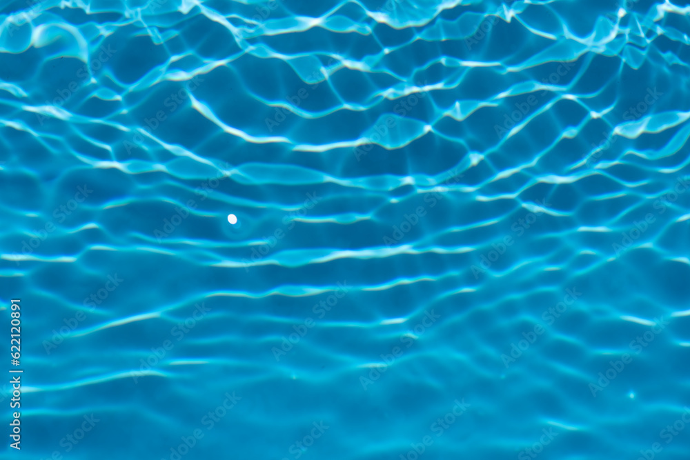 Blue water with ripples on the surface. Defocus blurred transparent blue colored clear calm water surface texture with splashes and bubbles. Water waves with shining pattern texture background.