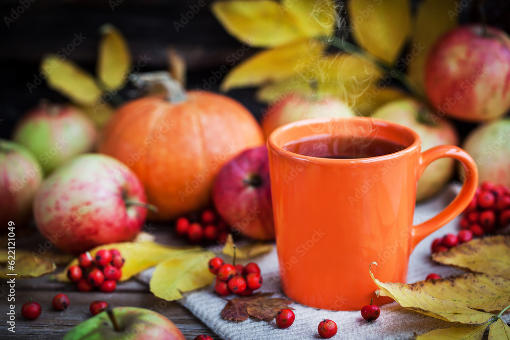 Orange mug on autumn background -fall leaves, apples, pumpkin and rowan-berry Orange mug on autumn background -fall leaves, apples, pumpkin and rowan-berry